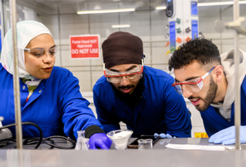 Three students working on an experiment in a lab Three students working on an experiment in a lab